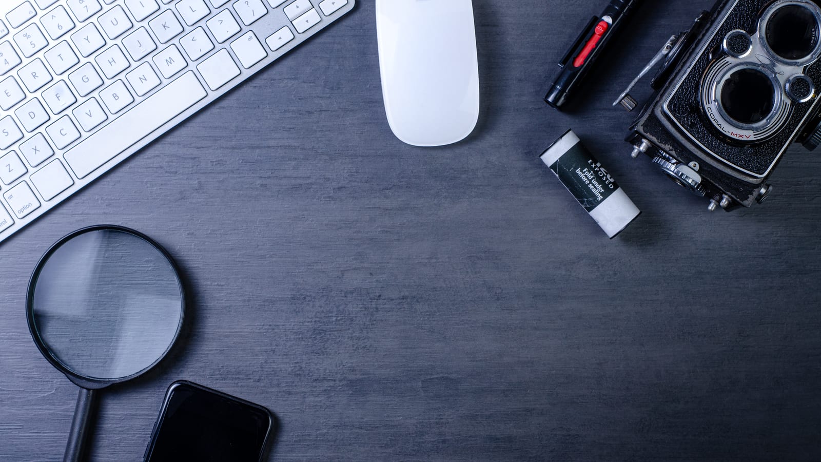 A magnifying glass, keyboard, mouse, and phone on a dark desk