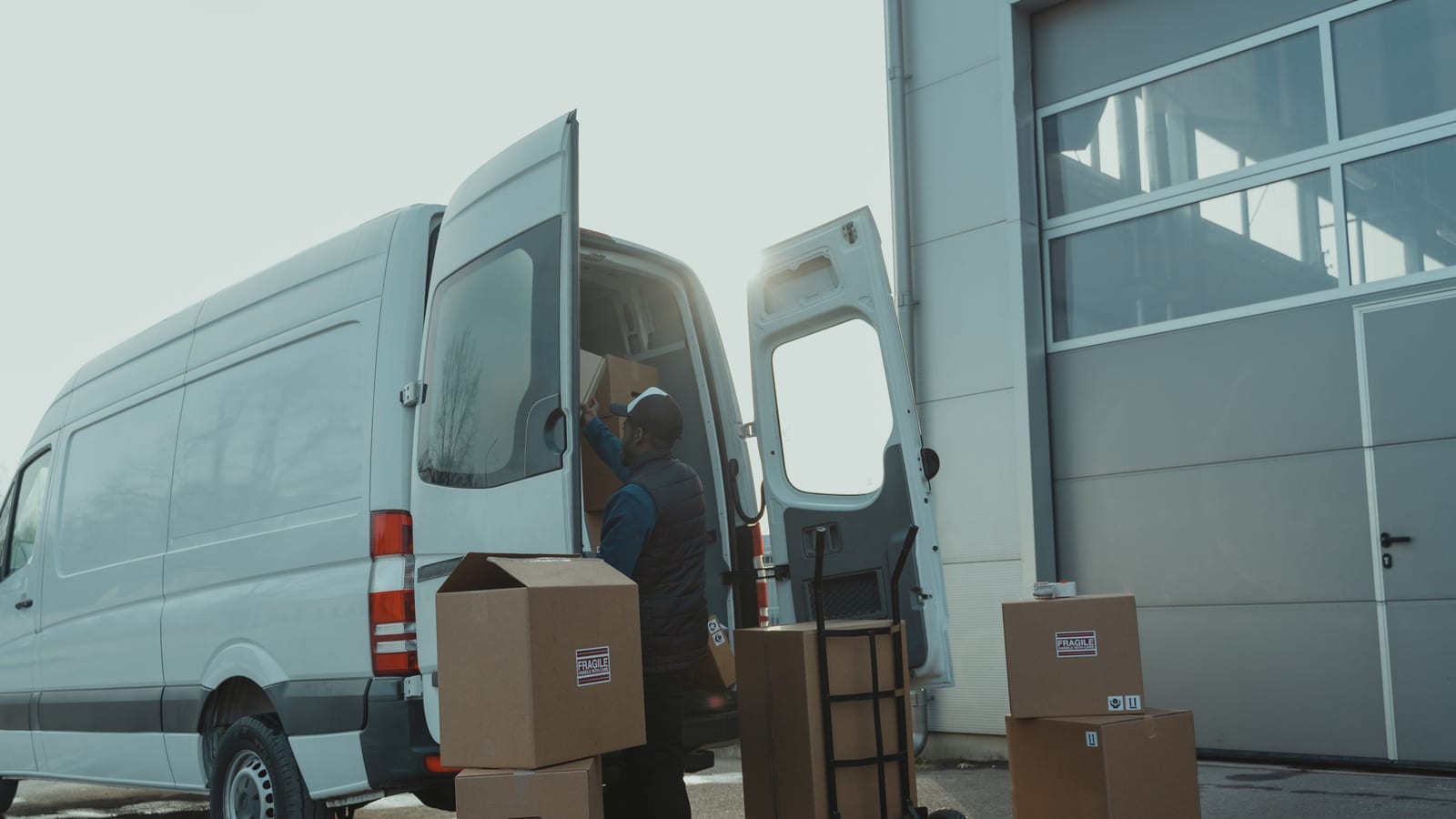A courier loading parcels into a delivery van outside a warehouse