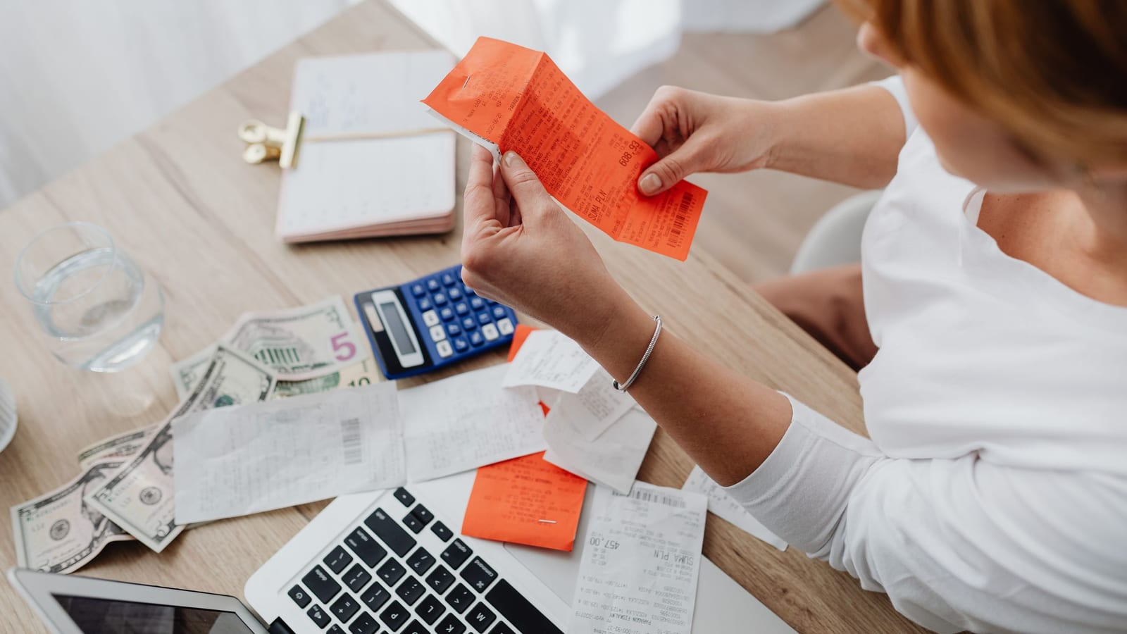 A woman sorting receipts next to a calculator and laptop at her desk