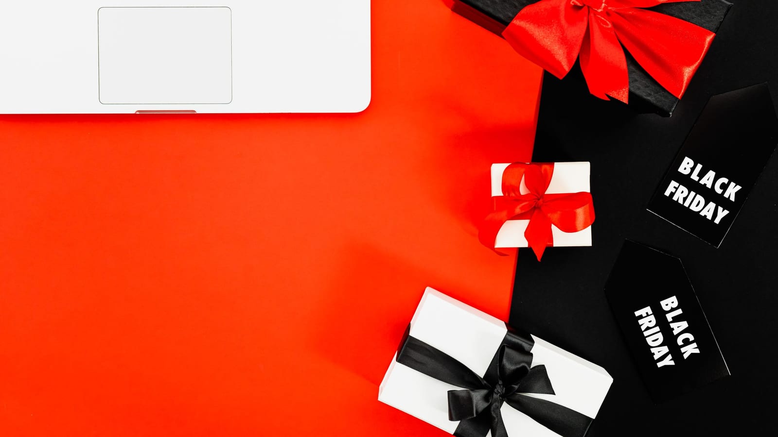 A laptop beside wrapped gift boxes and Black Friday tags on a red background