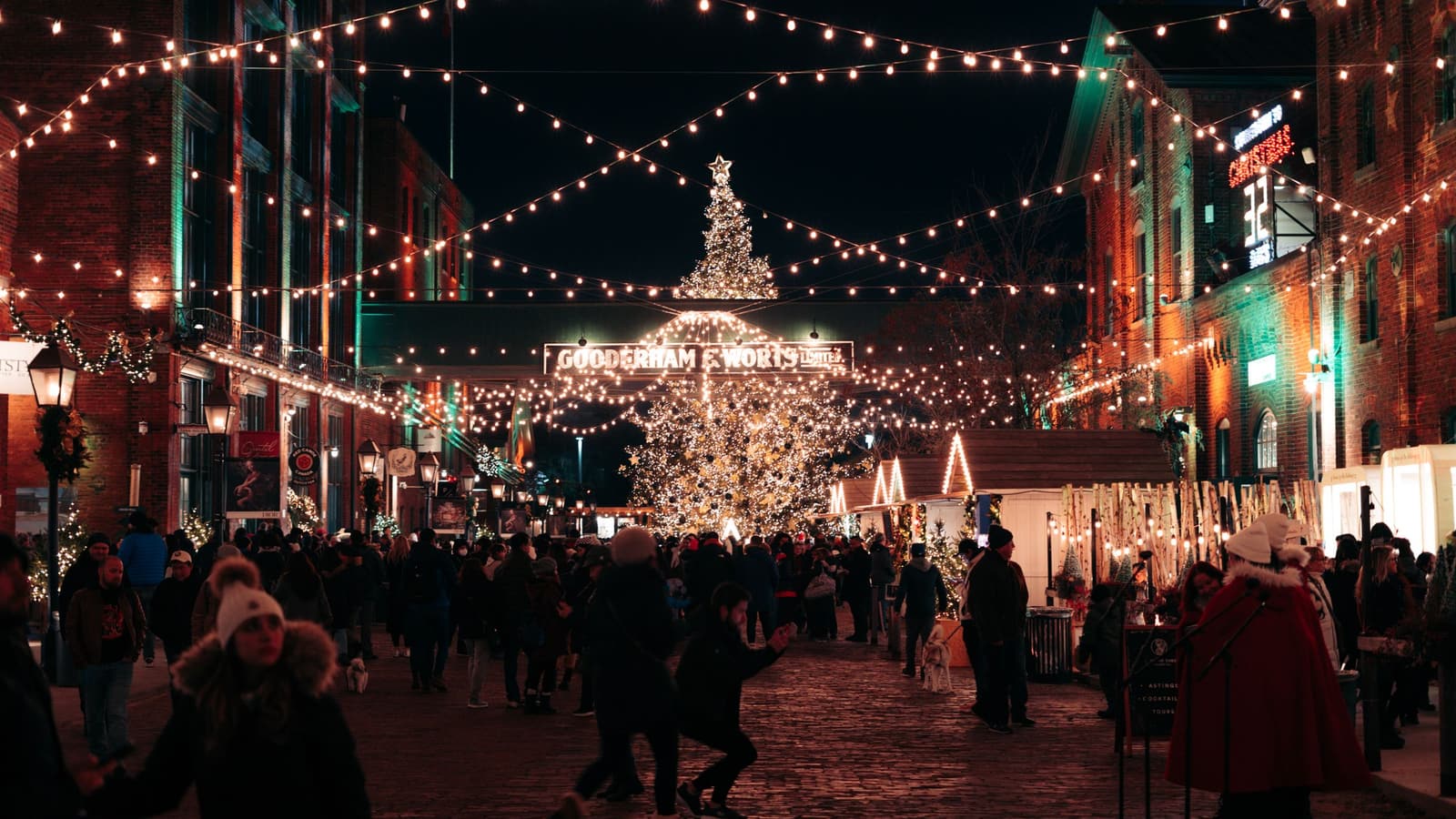 Shoppers at a busy Christmas market at night under string lights