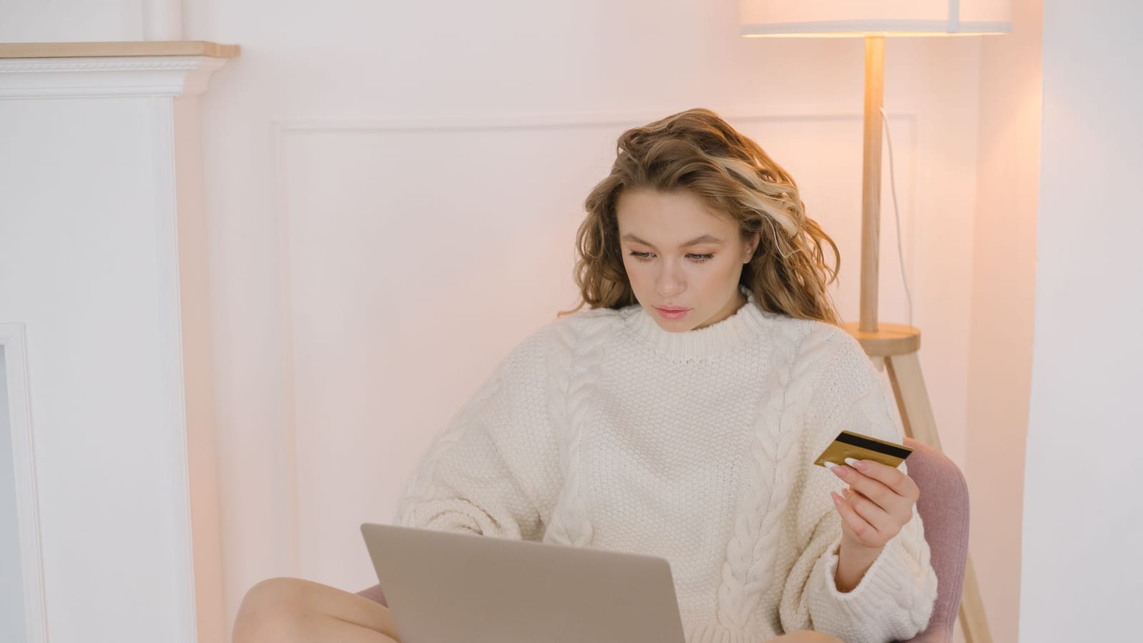 A woman in a sweater shopping on her laptop with a credit card