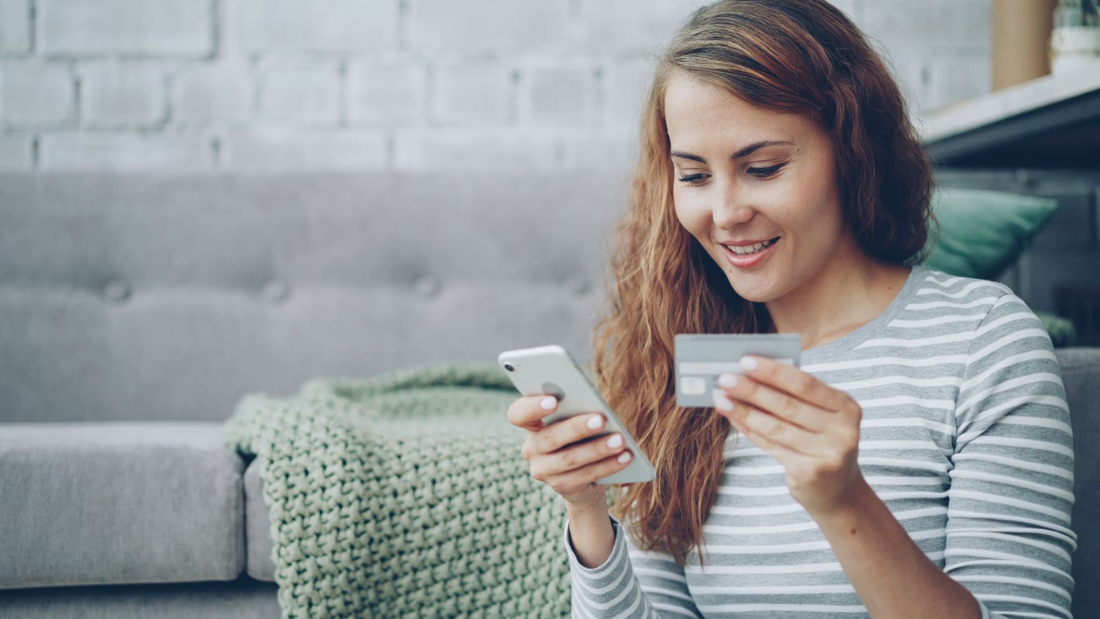 A woman shopping on her phone with a credit card in her other hand