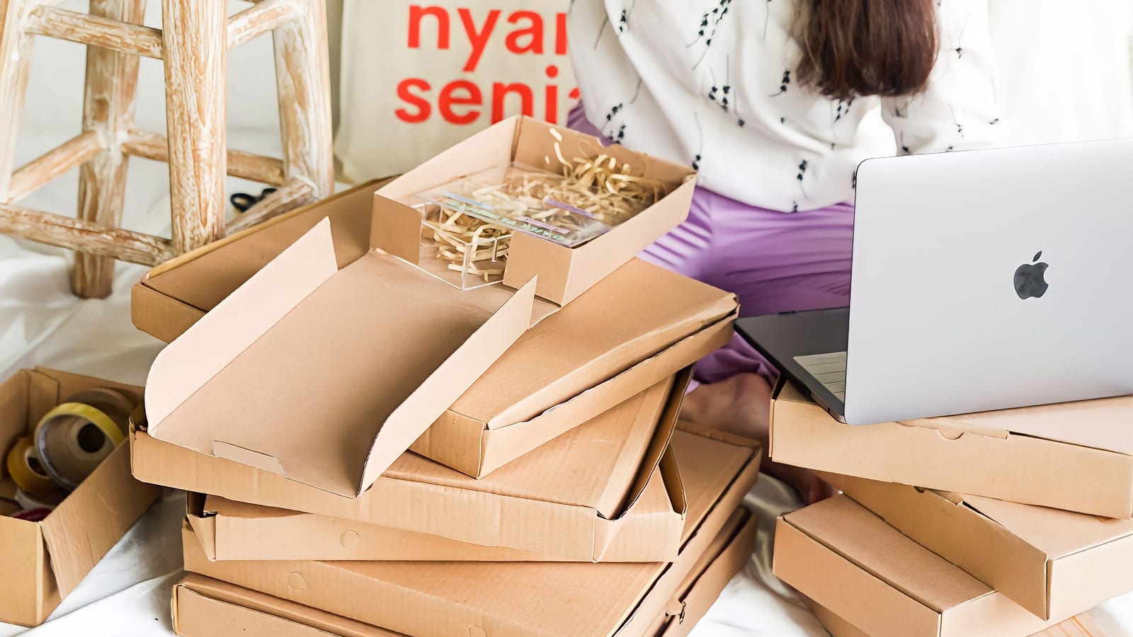 A small business owner packing orders into cardboard boxes next to a laptop