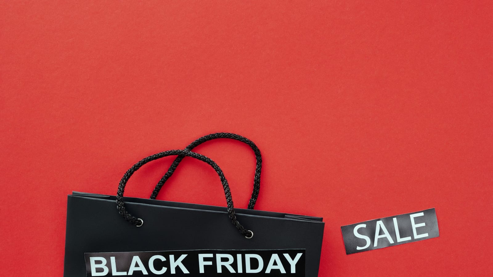 A black shopping bag with Black Friday and sale tags on a red background