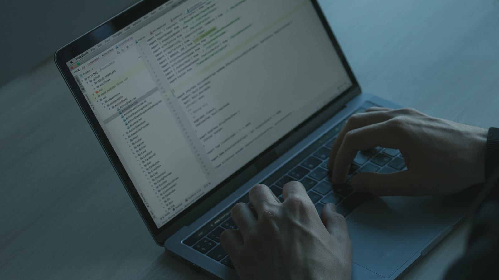 Hands typing code on a laptop in a dim room