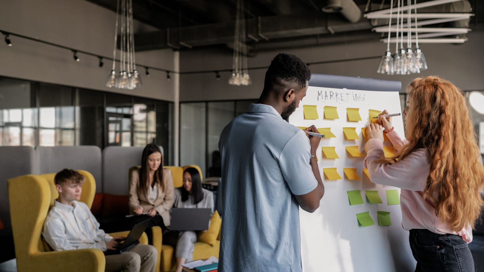 Two coworkers adding sticky notes to a whiteboard in an office