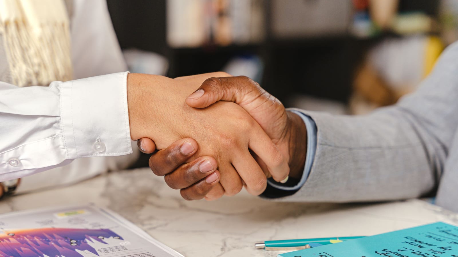 Two people shaking hands across an office desk