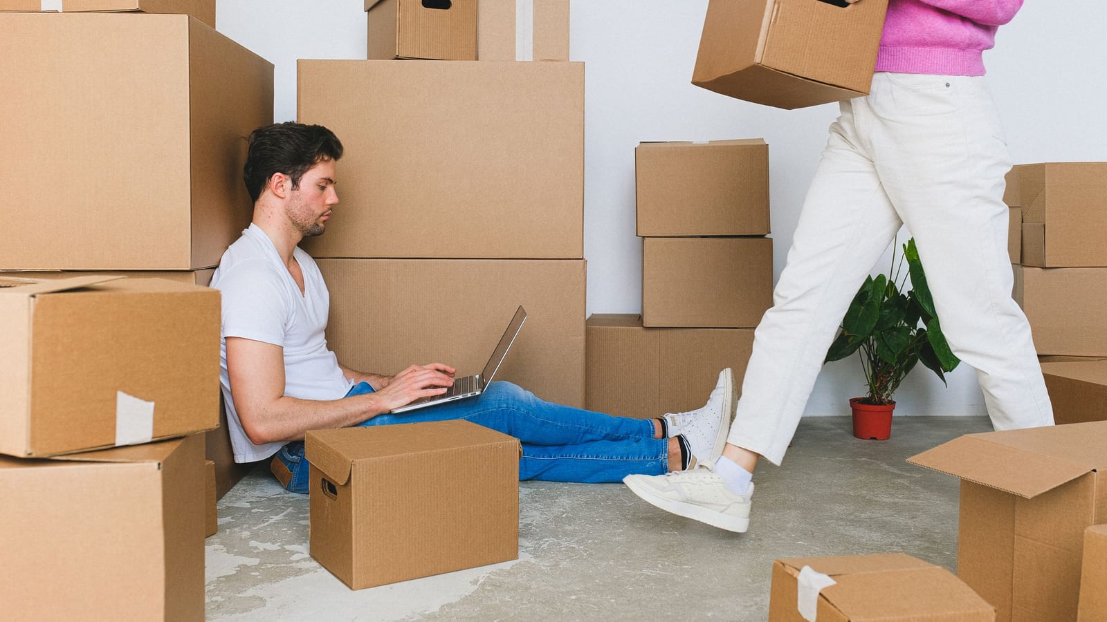 A couple surrounded by moving boxes, one working on a laptop